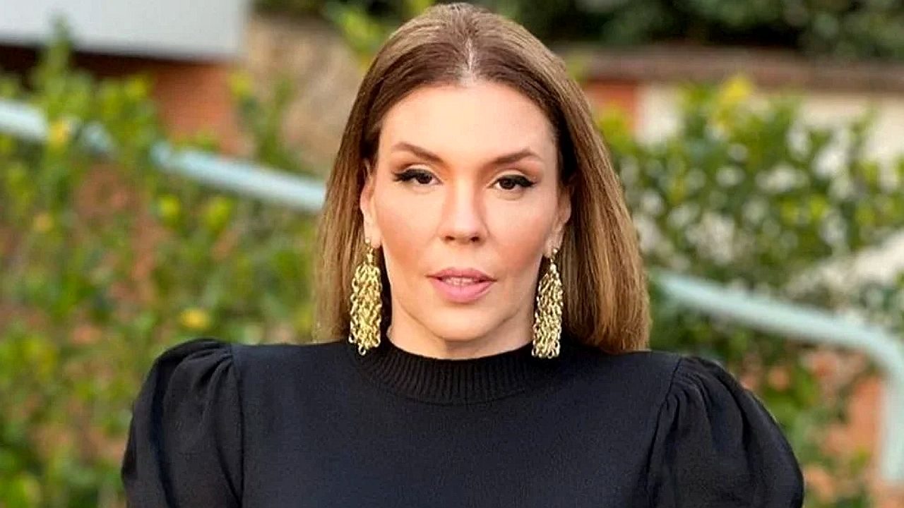 Mulher de vestido preto e brincos dourados posa ao ar livre em foto para entrevista ou programa de TV