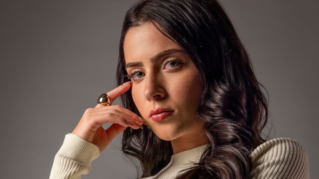 Jade Picon como Soraia na novela Tudo por Uma Segunda Chance com a mão no rosto usando anel dourado e blusa branca de gola alta