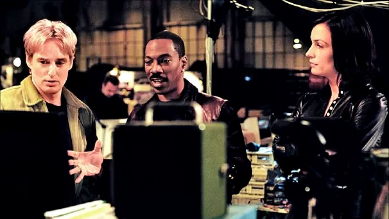 Owen Wilson, Eddie Murphy e personagem de Charlize Theron analisam monitor em cena do filme Sou Espião