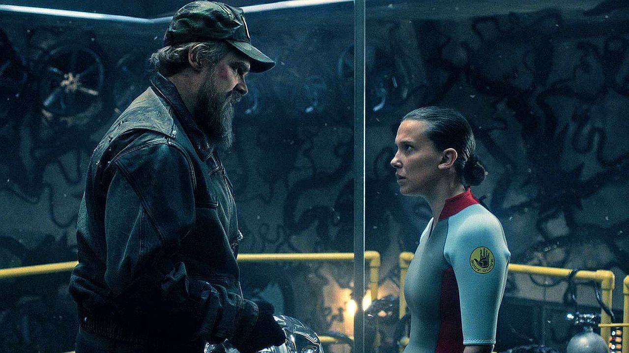 Homem de jaqueta e garota com uniforme encaram-se em laboratório subterrâneo em cena da série Stranger Things