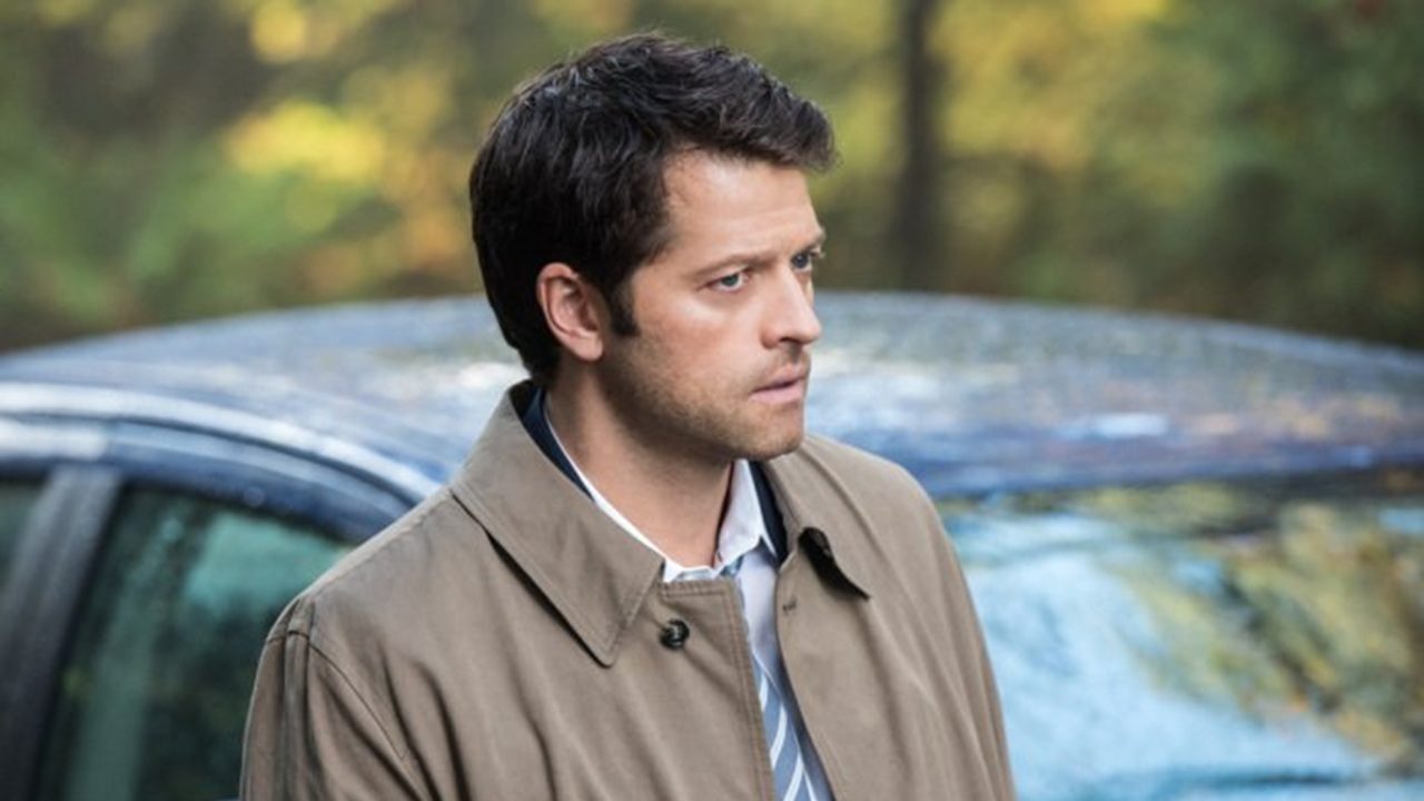 Homem de expressão séria está ao ar livre, usando sobretudo bege e camisa com gravata; ao fundo, vê-se um carro azul e vegetação desfocada.