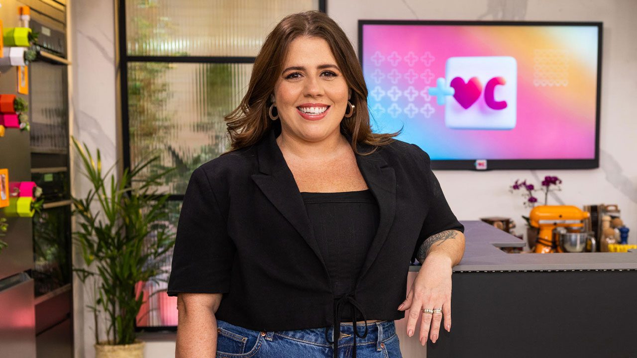 A apresentadora Tati Machado sorri com blazer preto no cenário do programa Mais Você, da Globo