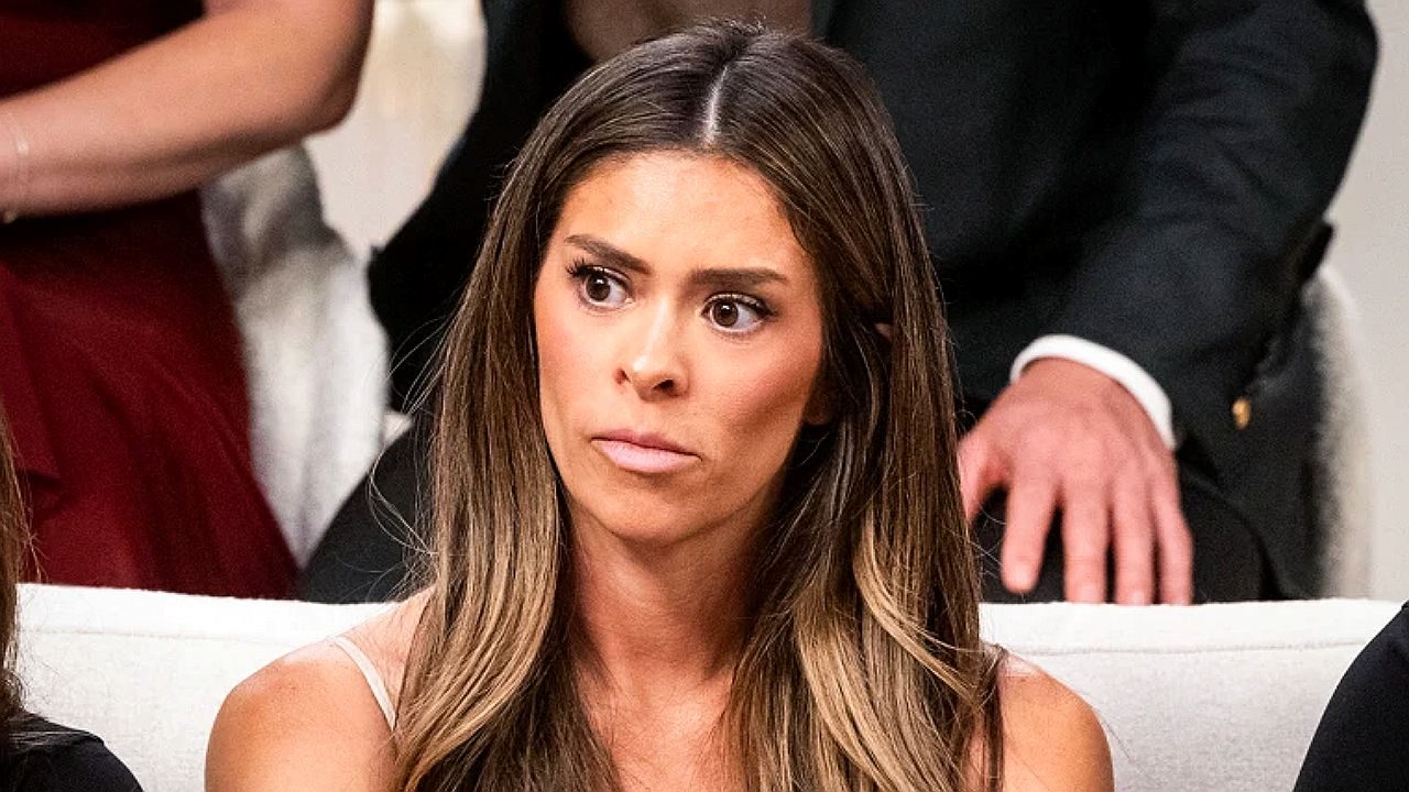 Mulher com expressão surpresa reage durante conversa sentada em sofá com outras pessoas ao fundo