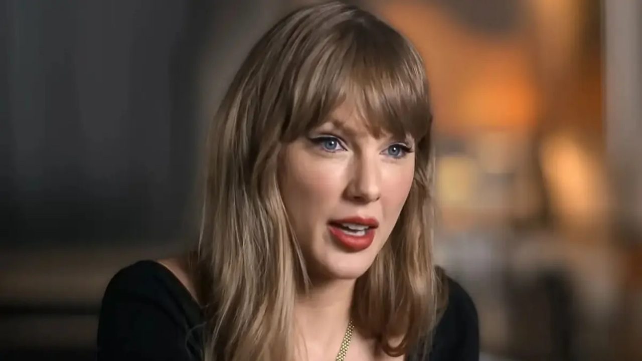 Taylor Swift fala em entrevista com blusa preta e franja em ambiente interno com iluminação suave