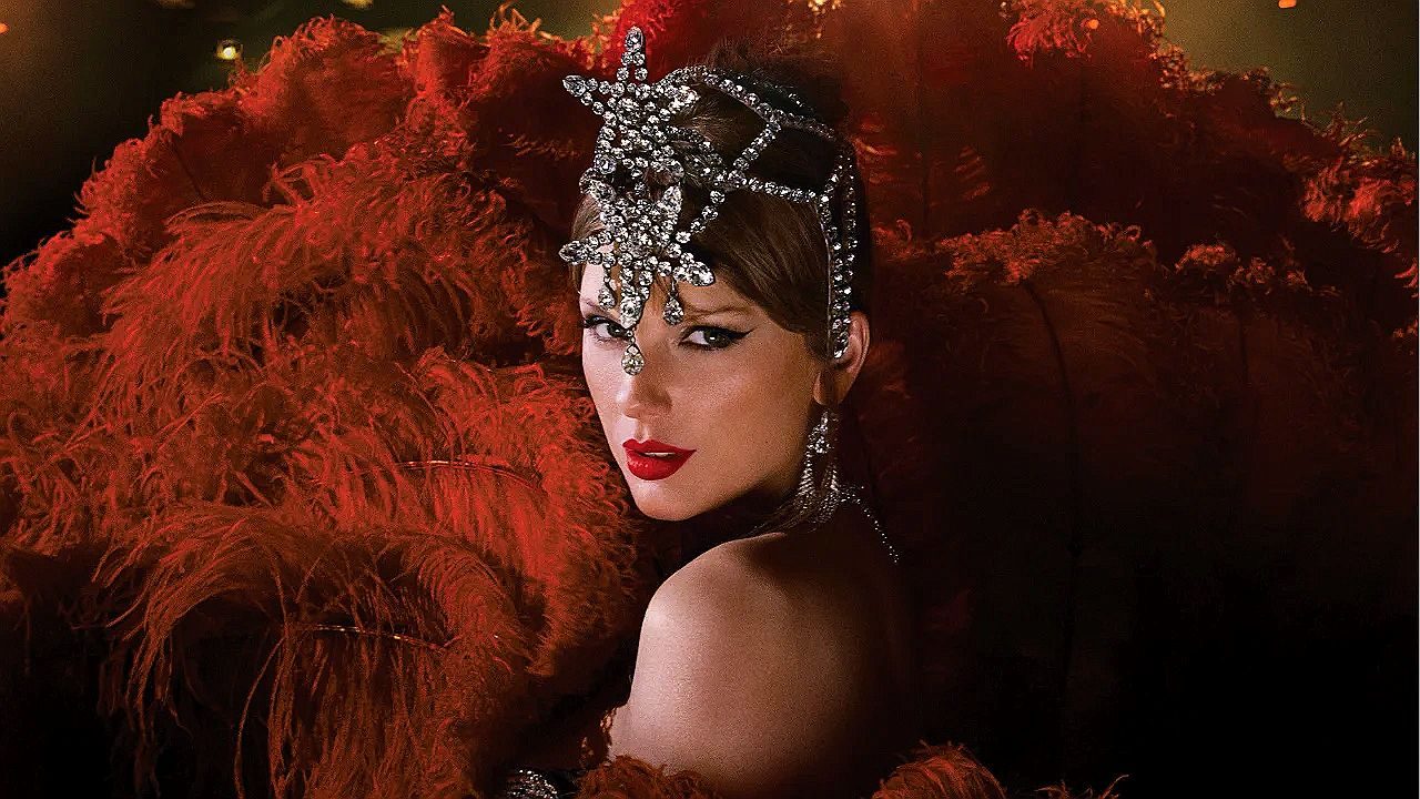 Taylor Swift com figurino de show, adereço brilhante na cabeça e plumas vermelhas durante apresentação musical