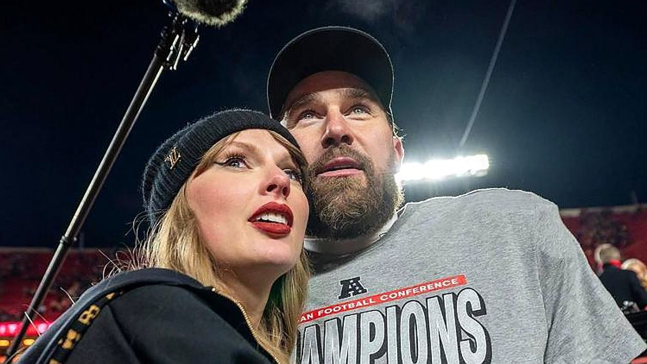 Cantora loira de gorro preto posa ao lado de homem barbudo com camiseta de campeão em estádio iluminado durante evento esportivo noturno