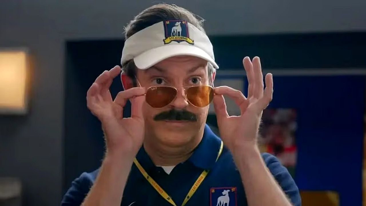 Ted Lasso ajusta os óculos escuros com viseira branca em cena da série de comédia da Apple TV+