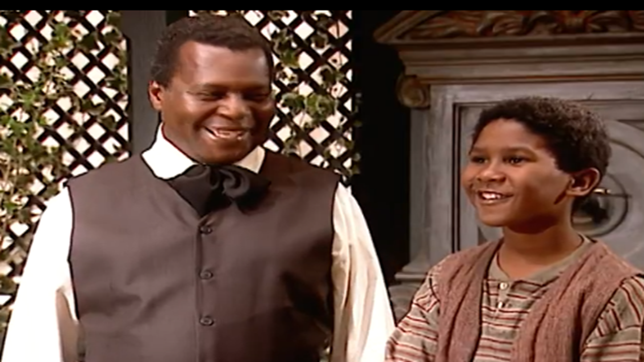 Cena da novela Terra Nostra mostra dois personagens sorrindo lado a lado em um ambiente com decoração clássica e plantas ao fundo