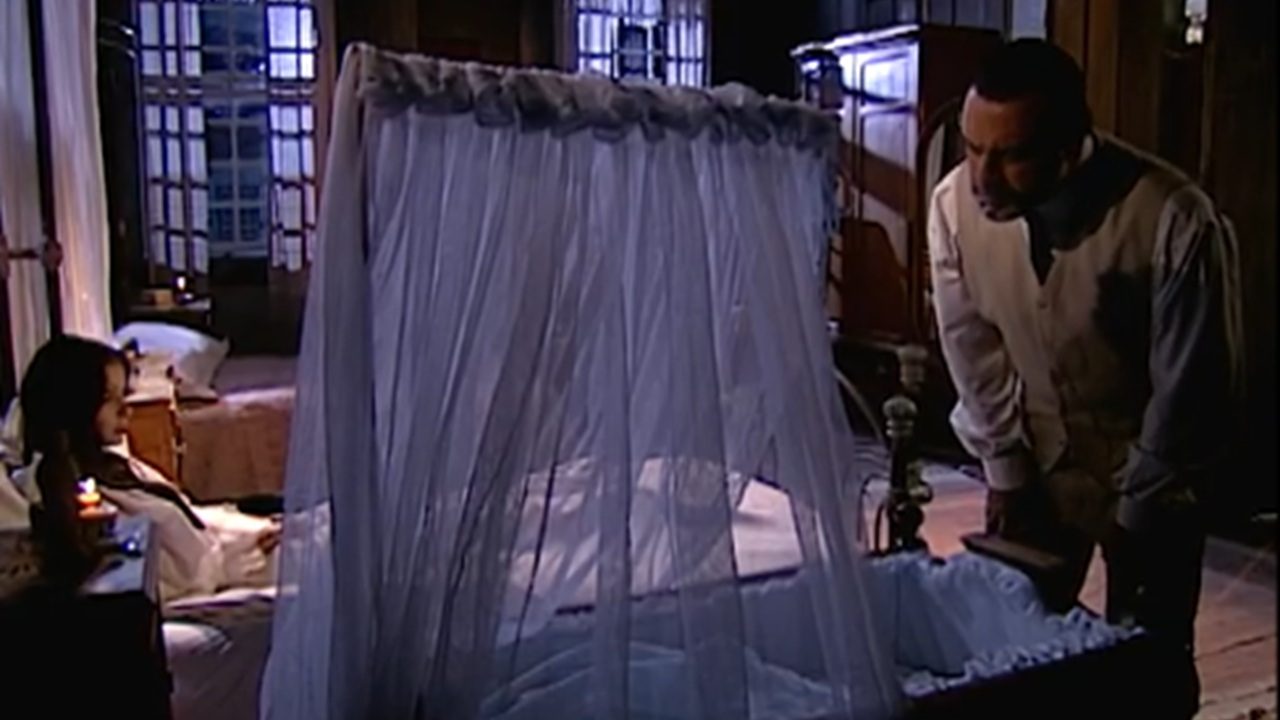 Angélica deitada na cama observa Gumercindo inclinado sobre o berço da neta em cena da novela Terra Nostra da TV Globo
