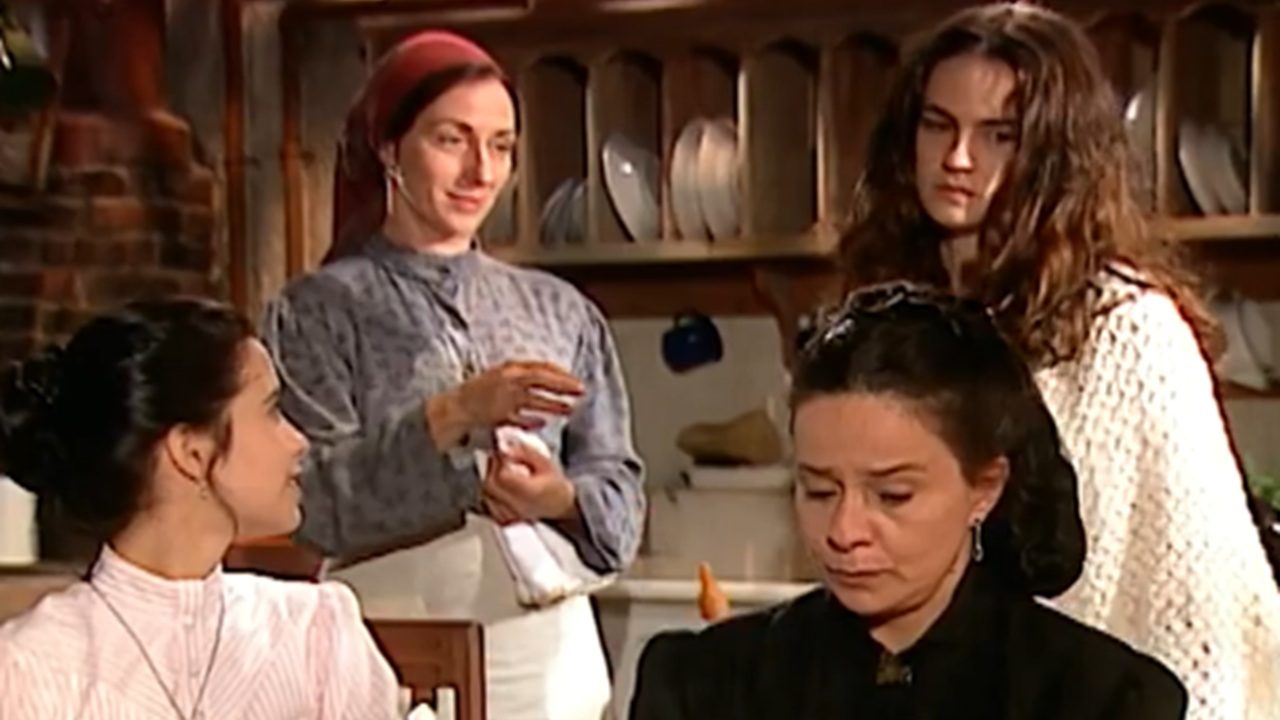 Cena de novela Terra Nostra mostra quatro mulheres em uma cozinha antiga, com expressões sérias e roupas tradicionais do início do século XX