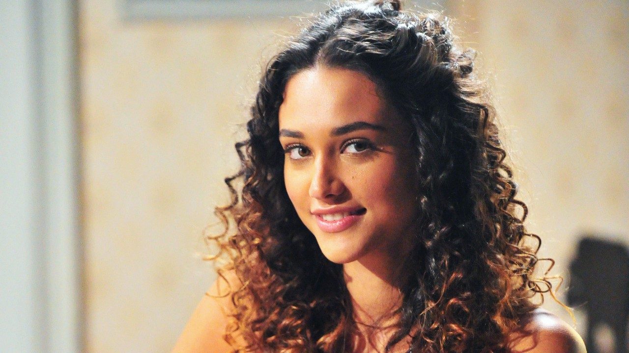 Débora Nascimento sorri como Tessália em cena da novela Avenida Brasil com cabelo cacheado solto e olhar para câmera