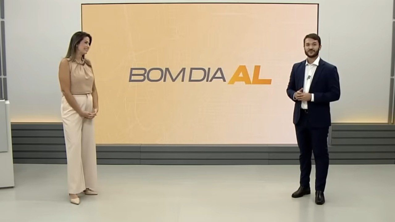 Thaíse Cavalcante e Ragi Torres apresentam o Bom Dia Alagoas em estúdio com telão ao fundo exibindo o nome do programa