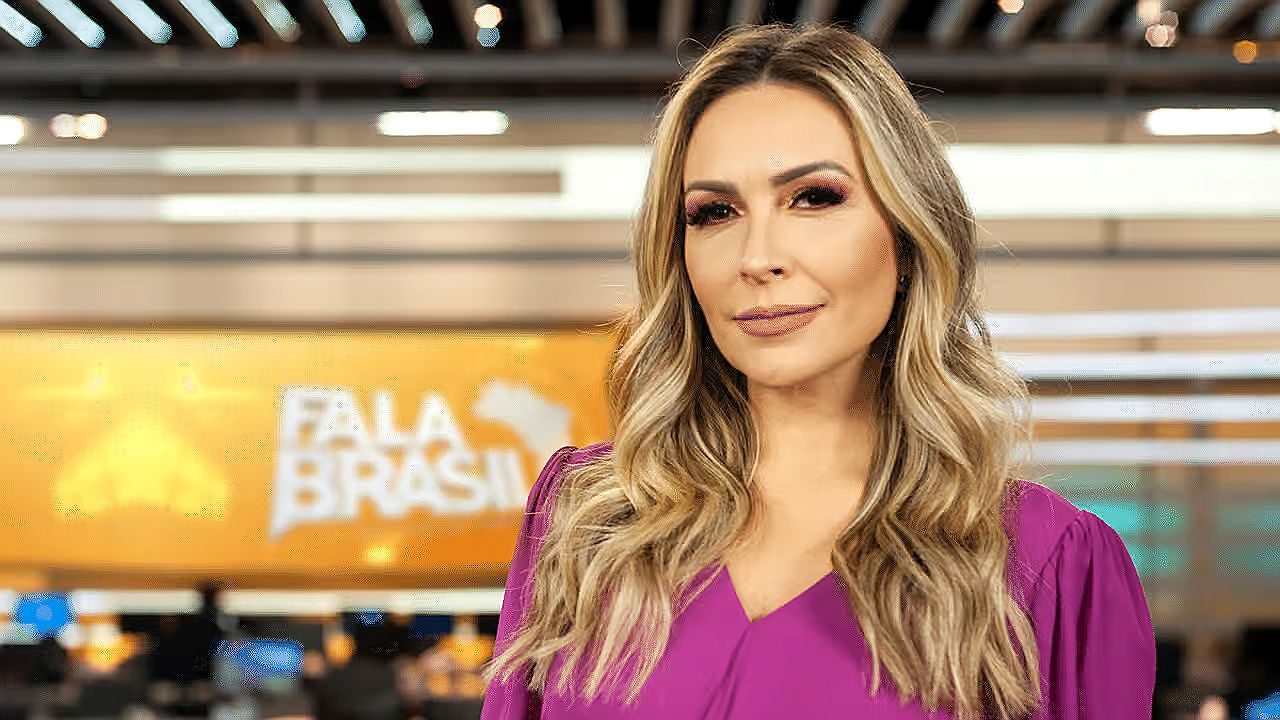 Thalita Oliveira posa na redação do Fala Brasil com vestido rosa diante do cenário do telejornal da Record TV