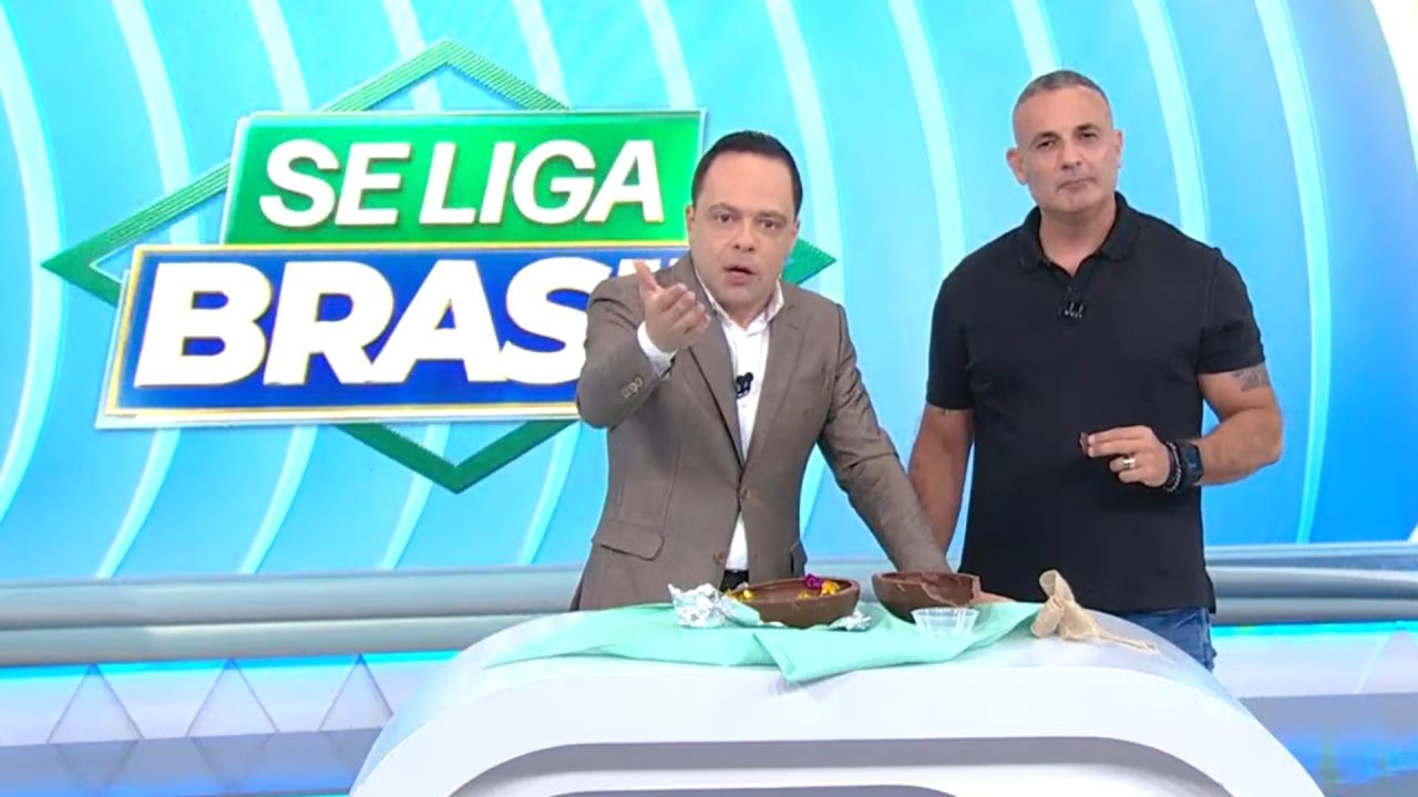 Thiago Gardinali e Mario Palumbo Junior, apresentadores do Se Liga, Brasil, mostram comida sobre bancada e falam no estúdio do SBT diante do telão do programa.