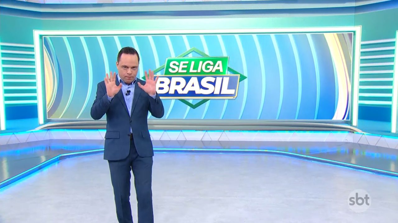 Thiago Gardinali gesticula no estúdio do Se Liga, Brasil, com telão exibindo logo do programa do SBT.
