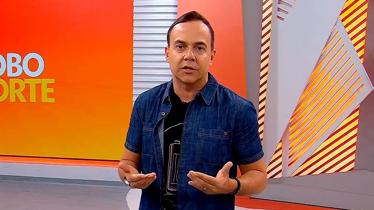 Apresentador fala no estúdio do Globo Esporte diante de telão laranja com identidade visual do programa