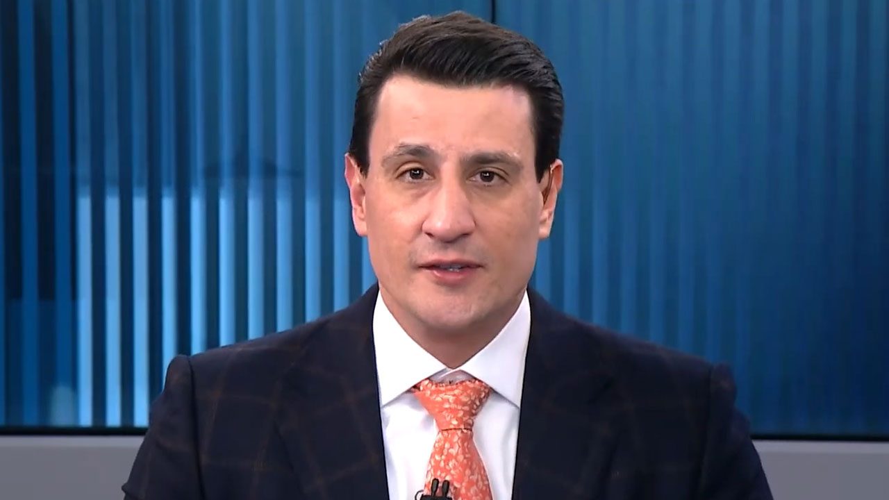 Tiago Pavinatto de terno e gravata laranja em enquadramento fechado no estúdio do programa Linha de Frente da Jovem Pan