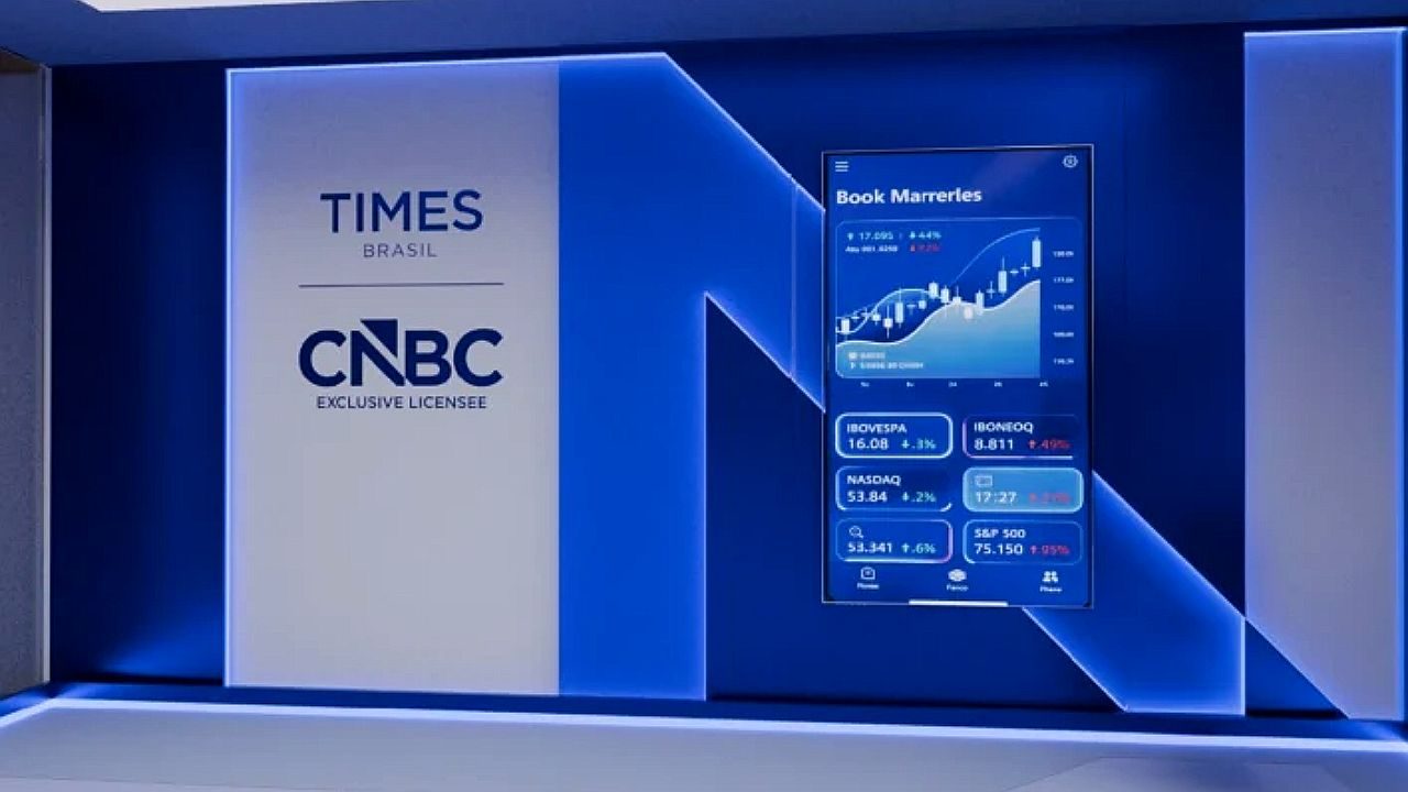 Logotipo Times Brasil CNBC em estúdio com tela exibindo gráfico financeiro e índices de mercado