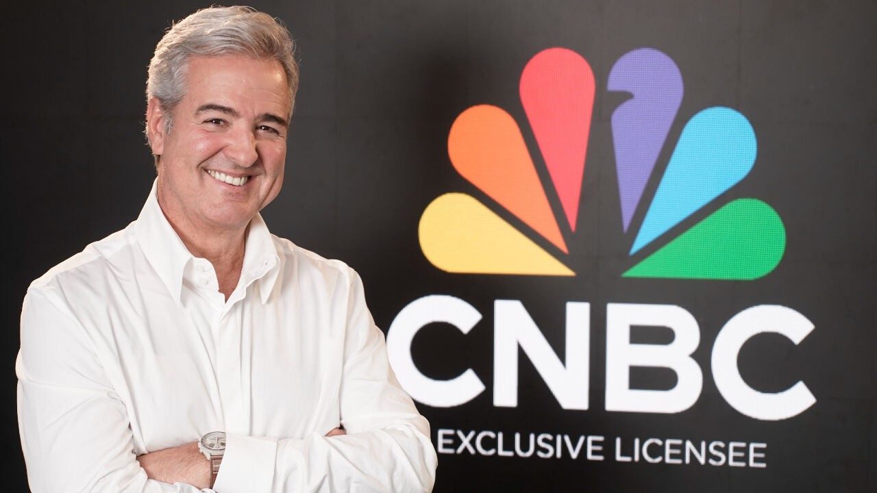 Thomaz Naves sorrindo em frente ao logo do Times Brasil CNBC com fundo preto e brasão colorido da emissora