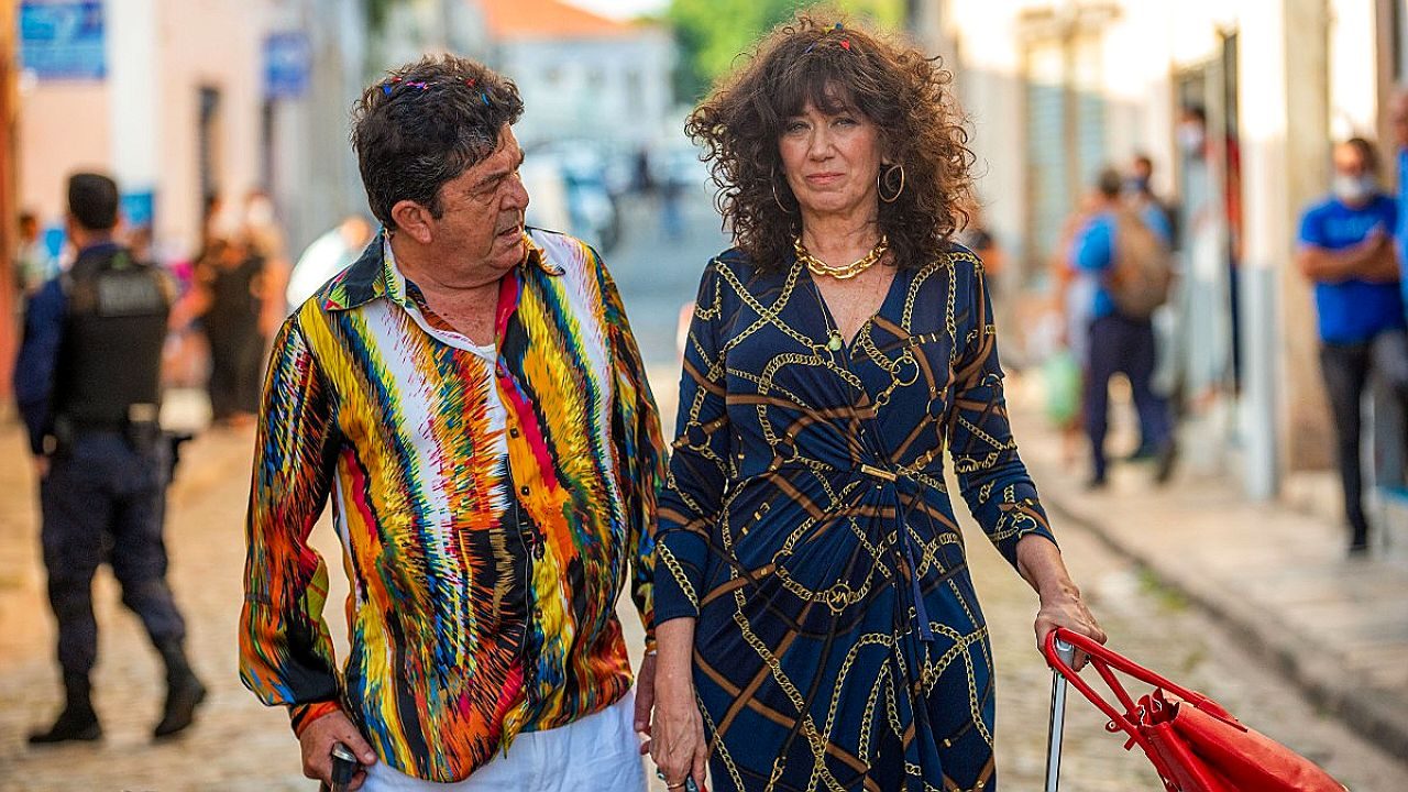 Texto Alternativo disse: Personagens de novela caminham por rua de cidade do interior enquanto conversam em cena gravada ao ar livre