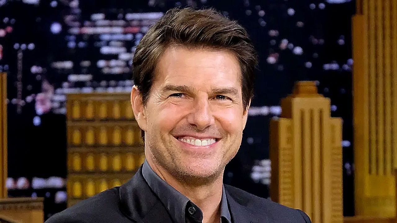 Tom Cruise sorrindo durante entrevista em programa de TV com cenário noturno ao fundo