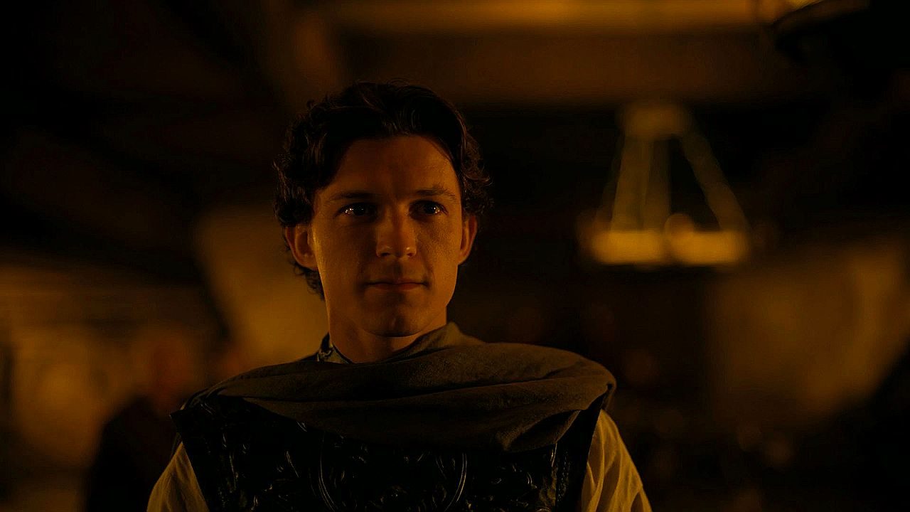 Tom Holland com armadura em cena de A Odisseia dentro de ambiente iluminado por luz baixa