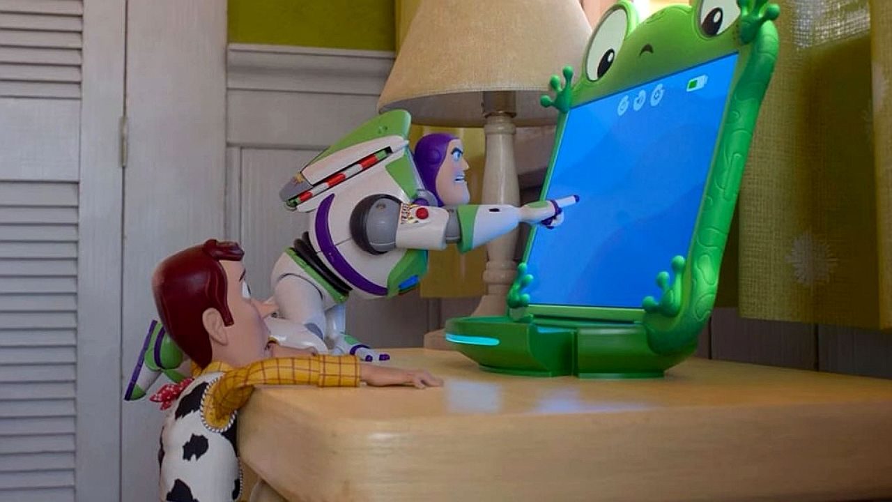 Woody e Buzz Lightyear observam computador infantil em formato de sapo em cena da animação Toy Story 5