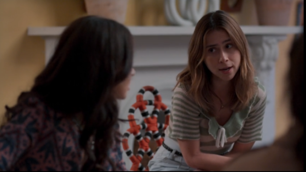 Mulher de blusa listrada verde conversa sentada com outras pessoas em sala decorada com lareira e vasos