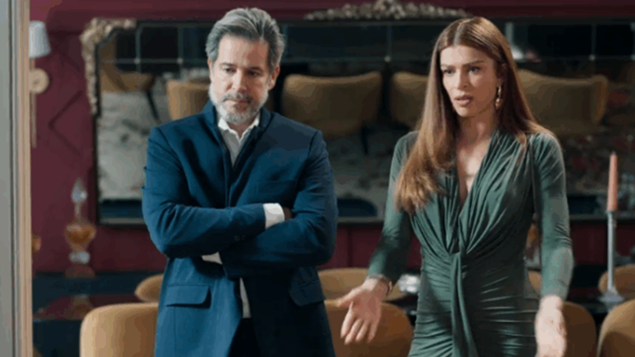 Homem de terno e mulher com vestido verde discutem em cena de drama ambientada em uma sala elegante