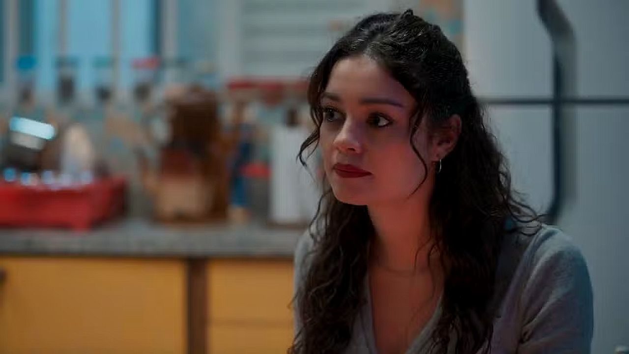 Mulher de cabelo cacheado olha atenta durante cena em cozinha com utensílios ao fundo