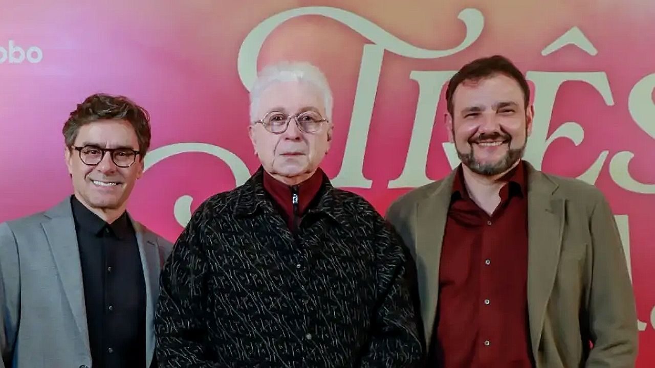 Três homens posam diante de painel rosa com nome da novela Guerreiros do Sol ao fundo