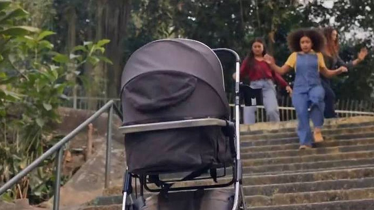 Carrinho de bebê parado em escadaria enquanto crianças correm ao fundo em cena de novela