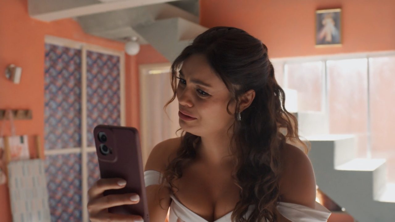 Gerluce observa celular com expressão preocupada em cena do último capítulo de Três Graças ambientada em quarto iluminado.