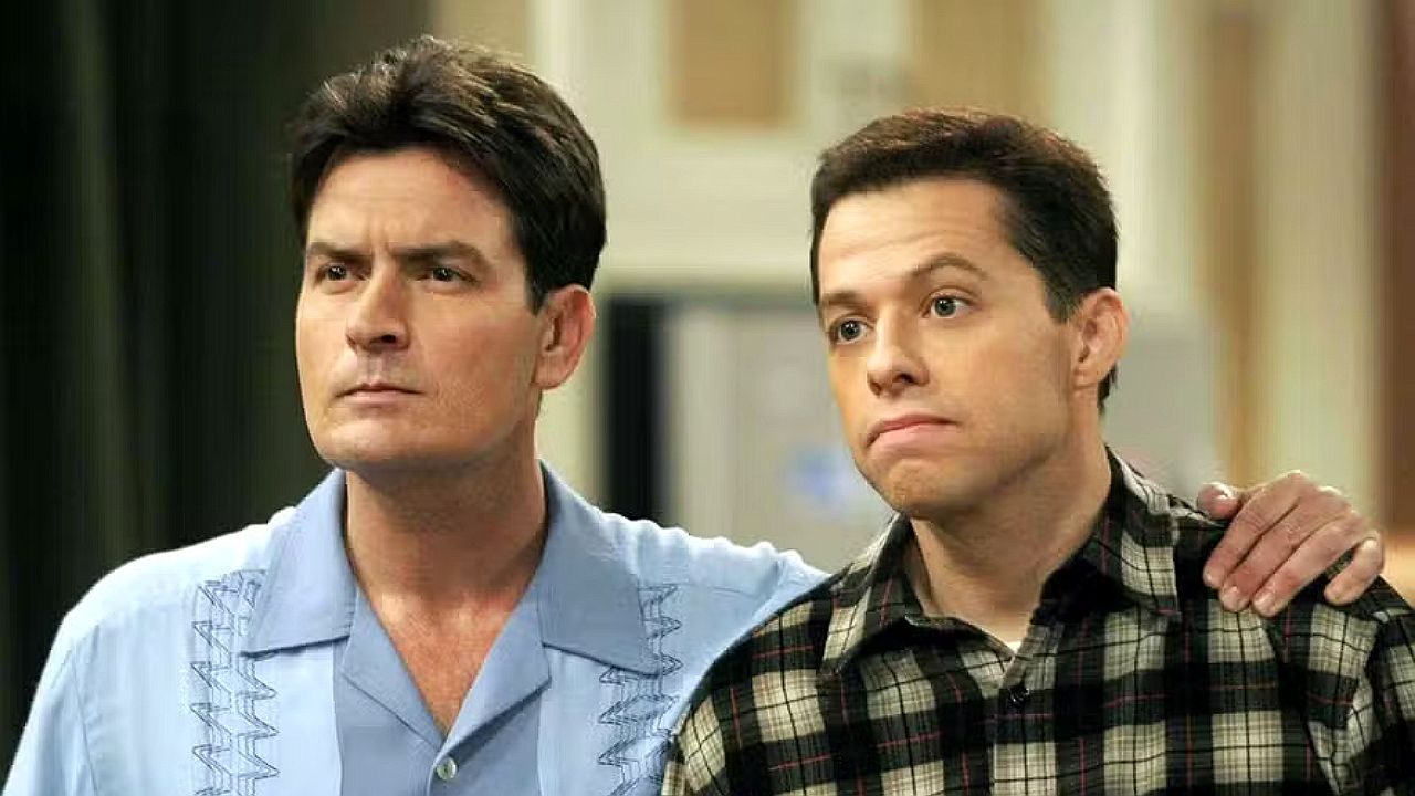 Dois homens lado a lado com expressão séria em cena de série, um com braço sobre o ombro do outro