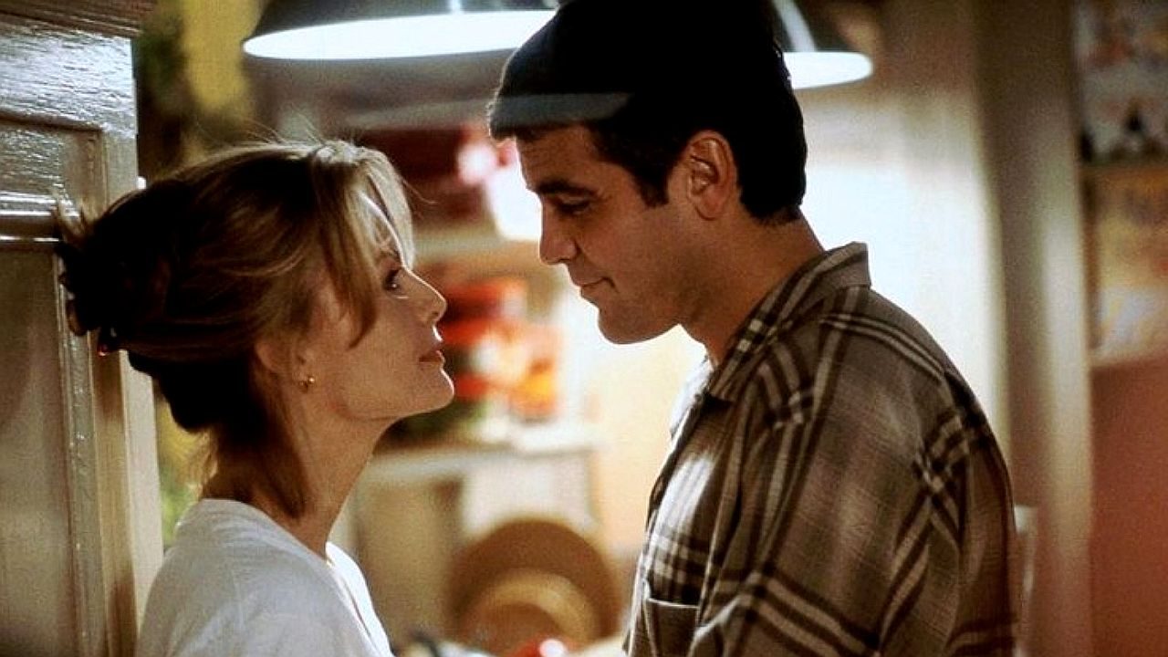 Casal se encara de perto em cozinha em cena de comédia romântica com clima intimista