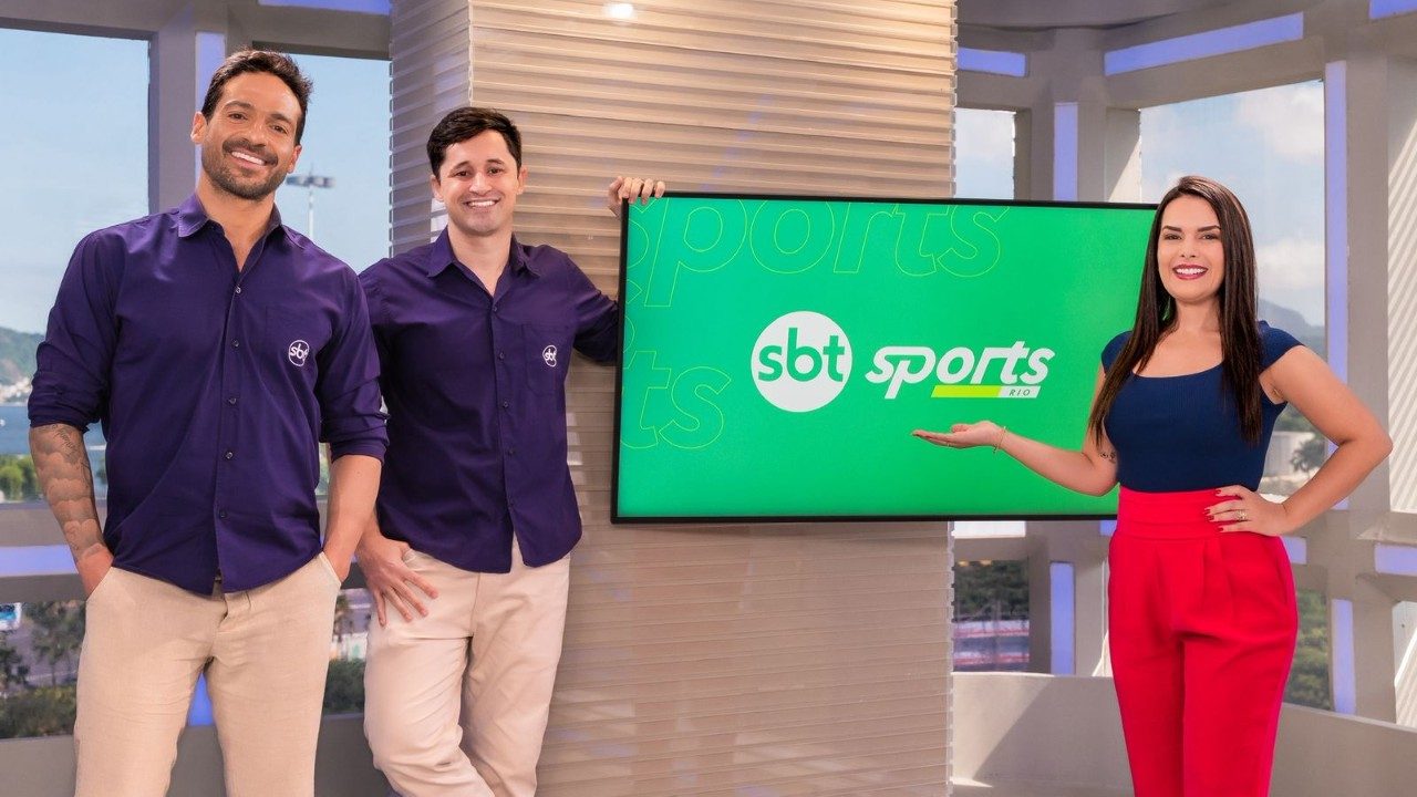 Venê Casagrande, Caio Caesar e Fernanda Maia sorriem lado a lado no cenário azul e branco do SBT Sports Rio, com logotipo do programa ao fundo