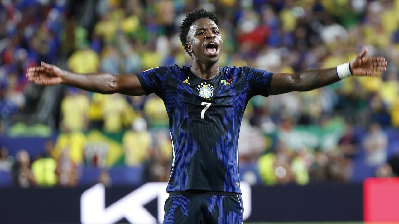 Vini Jr., de braços abertos e boca aberta, comemora gol com camisa azul da seleção brasileira diante da torcida nas arquibancadas durante partida contra o Haiti na Copa do Mundo