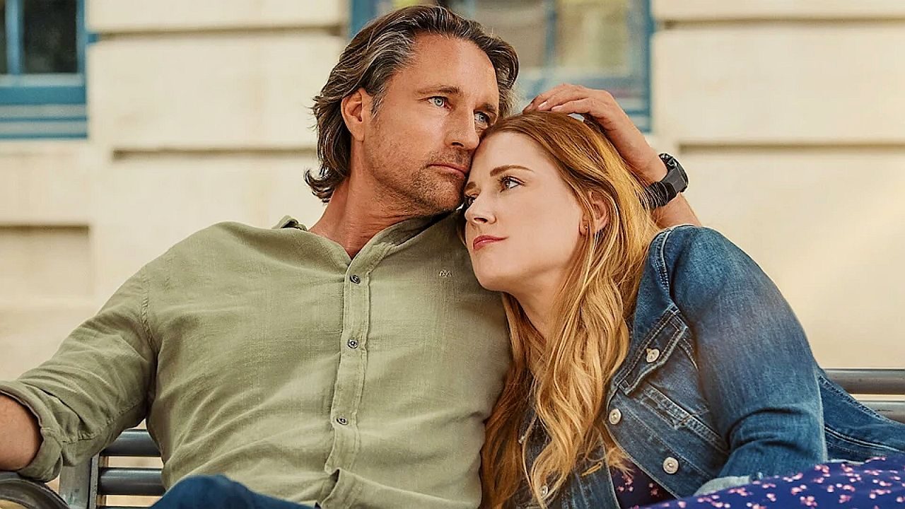 Homem abraça mulher que apoia a cabeça em seu ombro em momento romântico sentado em banco ao ar livre