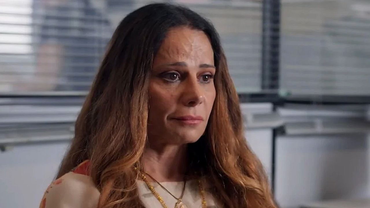 Viviane Araujo com olhar emocionado em cena de novela ambientada em escritório com persianas ao fundo