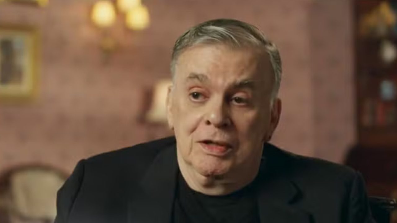 Walcyr Carrasco de blazer escuro fala durante entrevista em ambiente interno com iluminação suave e parede decorada ao fundo