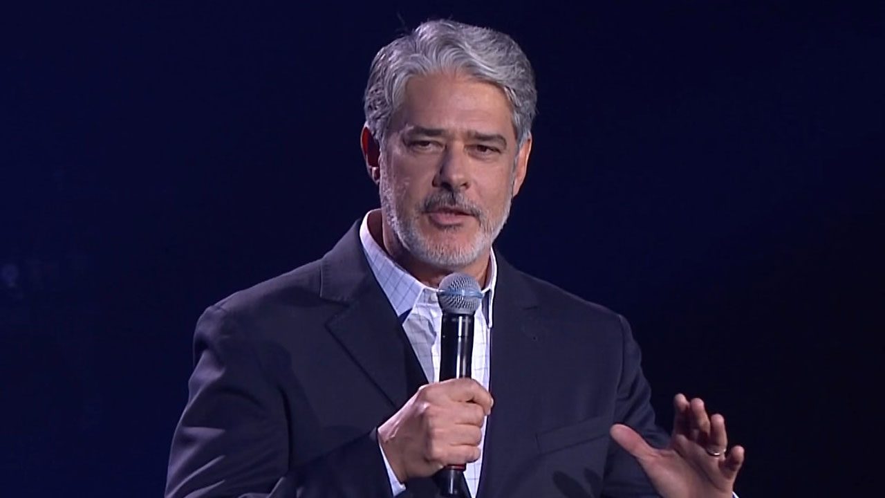 William Bonner, âncora do Jornal Nacional, com terno escuro e cabelo grisalho, fala ao microfone no palco do Upfront 2026 da Globo