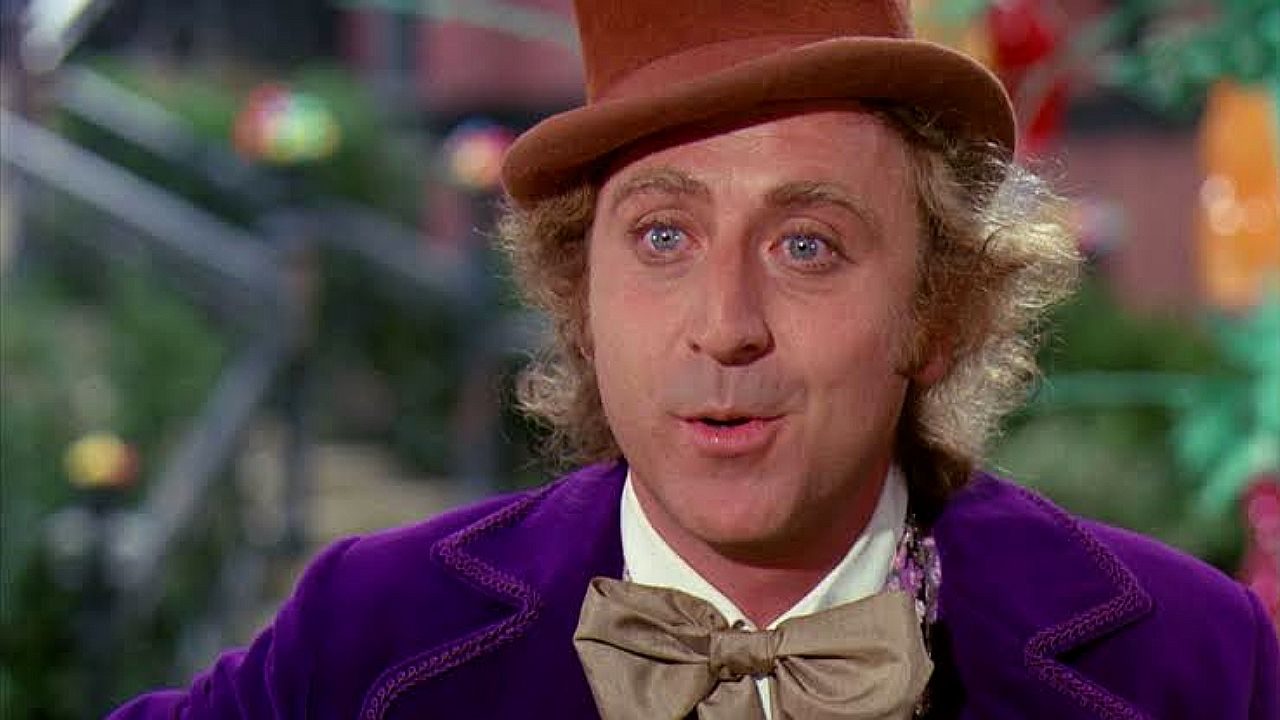 Willy Wonka com cartola marrom e casaco roxo em cena clássica de A Fantástica Fábrica de Chocolate