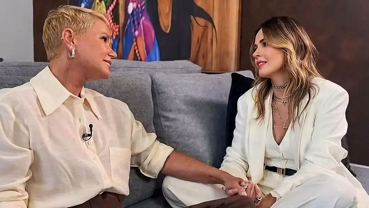 Duas mulheres conversam sentadas no sofá e dão as mãos durante entrevista em programa de TV