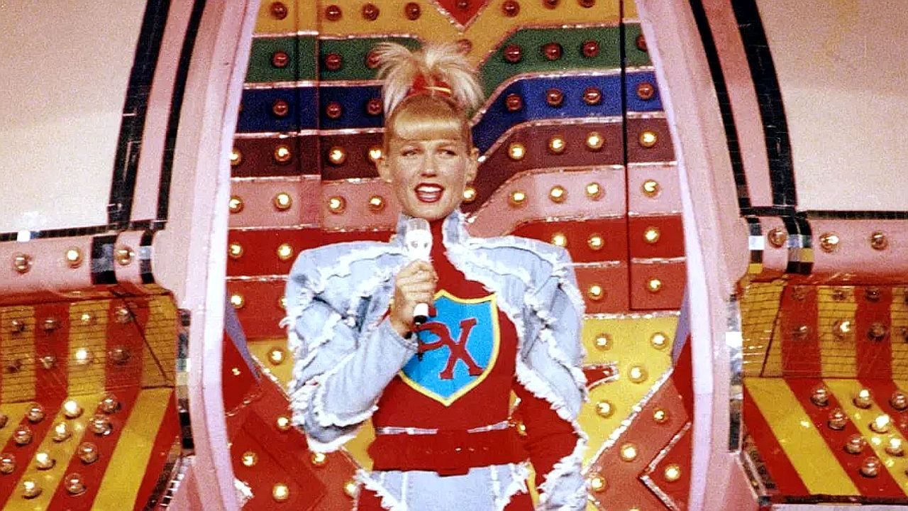 Xuxa canta com microfone em palco colorido durante apresentação do programa Xou da Xuxa