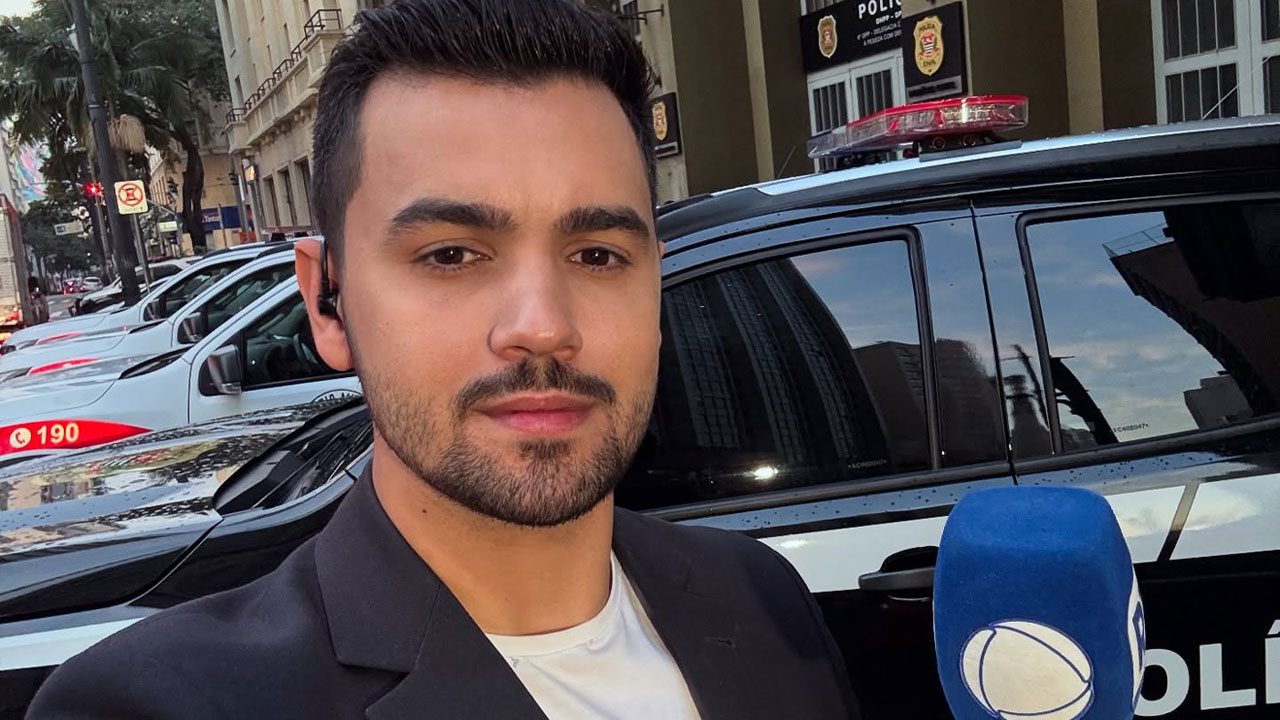 Yuri Macri com microfone da Record em frente a viatura da polícia civil durante reportagem na rua