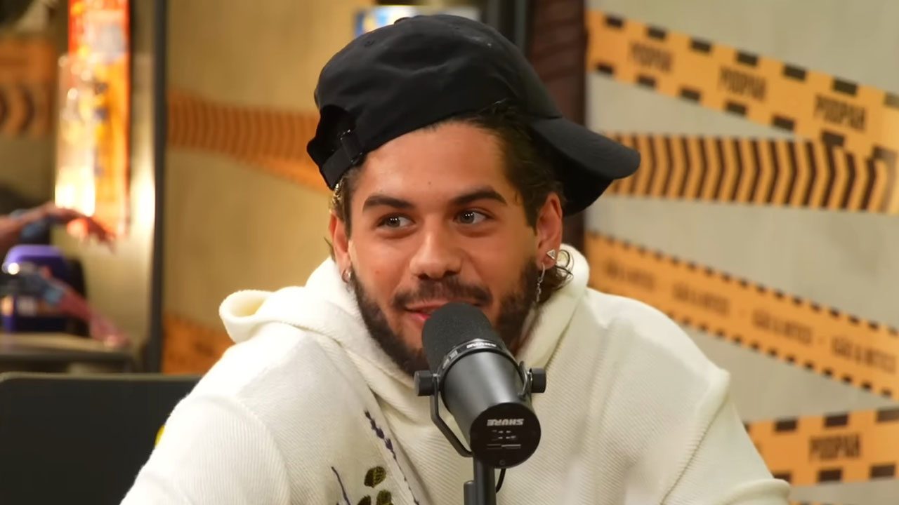 Cantor Zé Felipe com barba e boné preto, sorrindo e falando em microfone de podcast no estúdio do Podpah