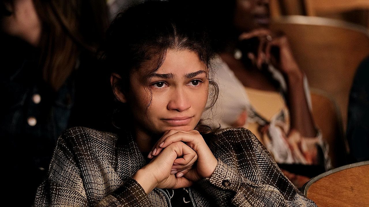 Mulher com expressão emocionada e olhos marejados apoia o queixo nas mãos em cena de série dramática